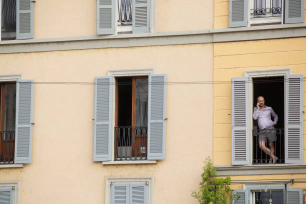 Milan, Italy, June 9, 2023: Exterior view of building with grey timber window shutters and a male on his mobile phone in the window on Cathedral Square, the main city square in Milan
