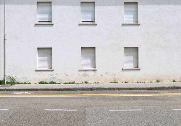 istock White plaster building with closed white shutters.Concrete sidewalk, bicycle lane and urban street in front. 2158943902