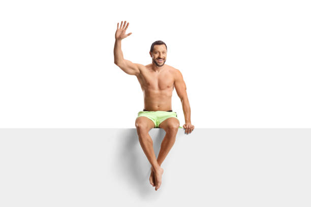 Man in swimwear sitting on a panel and waving isolated on white background