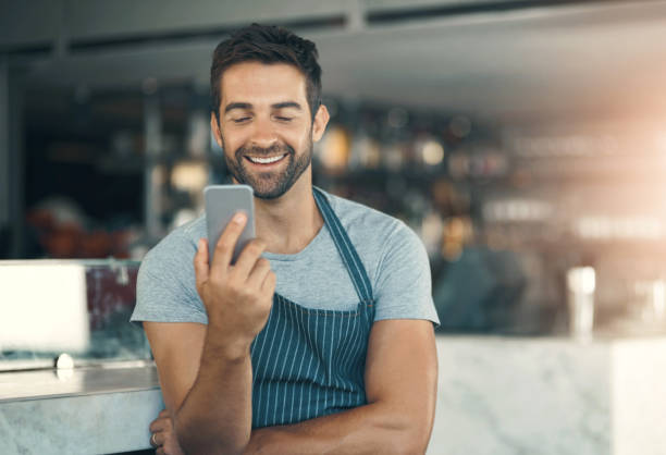 istock Barista, man and mobile phone in cafe with apron for  communication, networking or restaurant app. Connection, small business owner and male person for social media, browsing internet or online order 2158944985