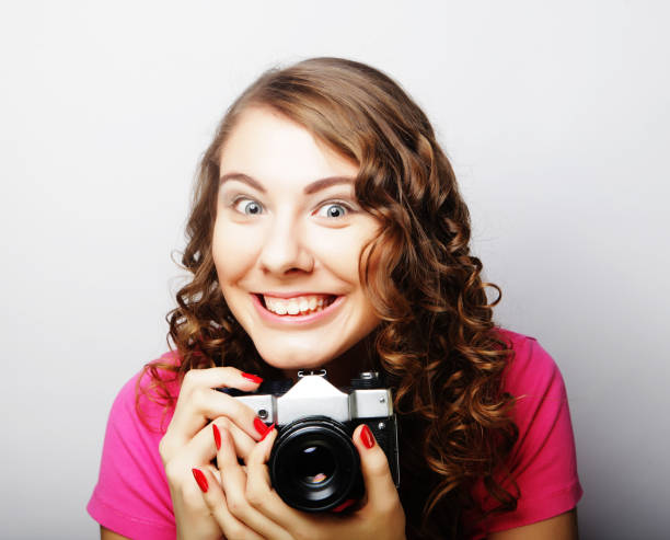 young pretty woman holding vintage camera over gray background.