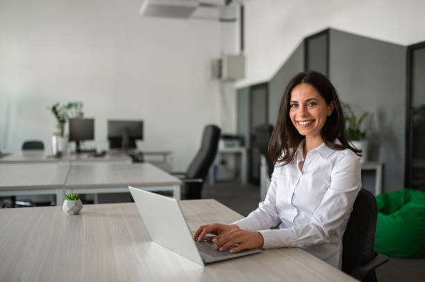 istock Young female entrepreneur smiling and working on her lap top in modern workspace 2158956747
