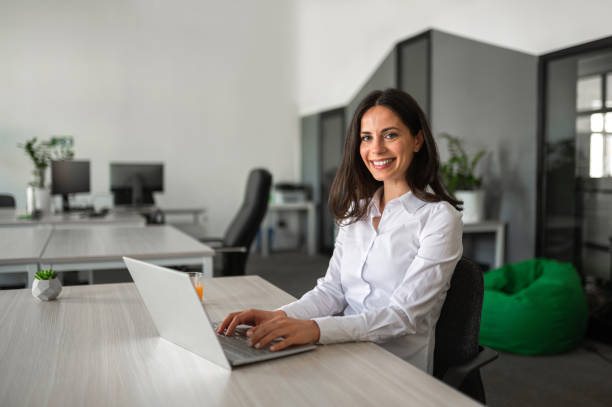 istock Young business person smiling and working on her lap top in modern workspace 2158956760