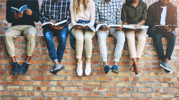 Students, group and books on wall with legs, learning and reading for development at college. People, friends and scholarship for education, information and knowledge for future at university campus
