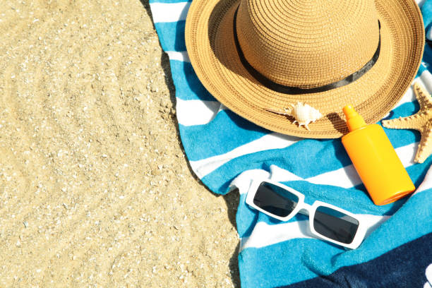 istock Beach essentials on towel, yellow sunscreen bottle, stylish sunglasses and hat. Top view 2158956989