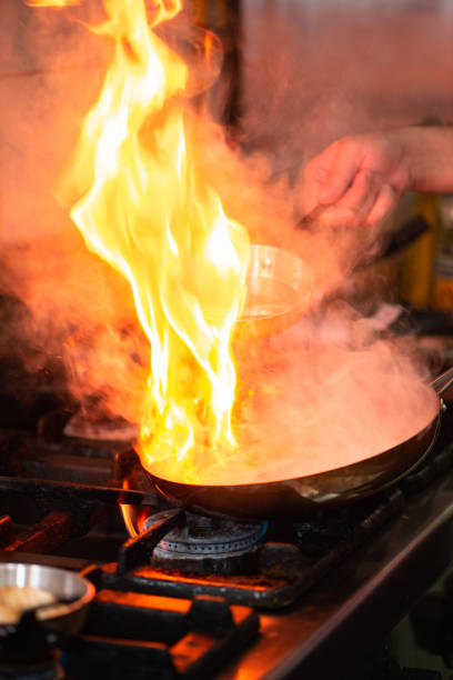 Close-up shot of unrecognizable young chef and sous-chef cooking food with burning fire in the kitchen in restaurant kitchen
