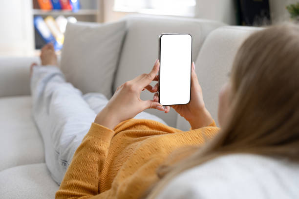 istock A woman holding mobile phone with blank white screen while lying on a sofa at home 2158961976