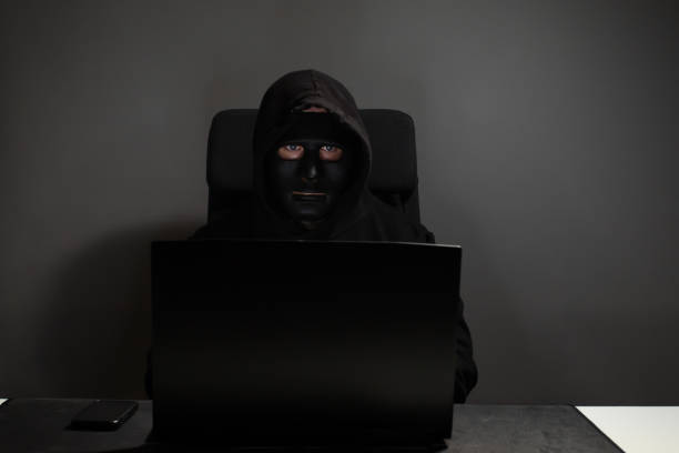 istock Hacker, man in mask with laptop, executing a phishing scam, obtaining passwords, compromising privacy. 2158964696