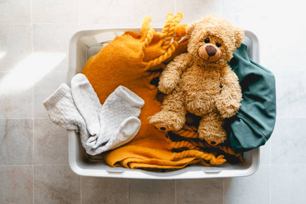 A laundry basket with dirty laundry and a teddy bear