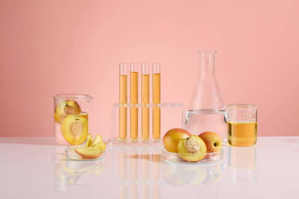 istock The creative photo on pink background of peach fruit and laboratory concept. Experiment tools placed on the white table, with pieces of peach fruits and yellow liquid contained in. Front view photo 2158968489