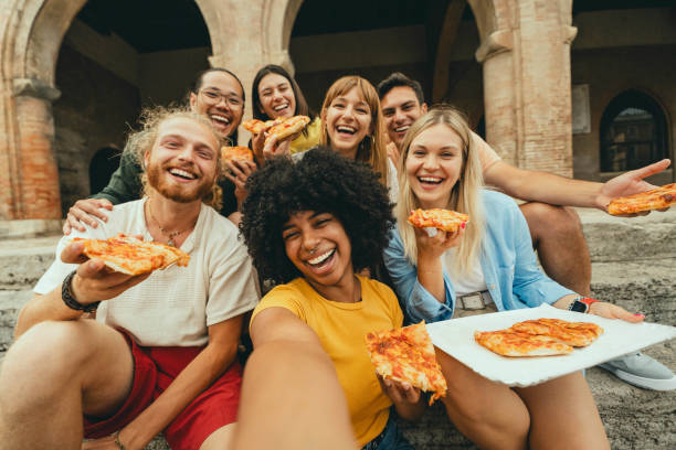 istock Multicultural smiling friends eating pizza sitting outside - Cheerful young people taking selfie photo with smartphone outdoor - Happy life style concept with guys and girls hanging out on a sunny day 2158975563
