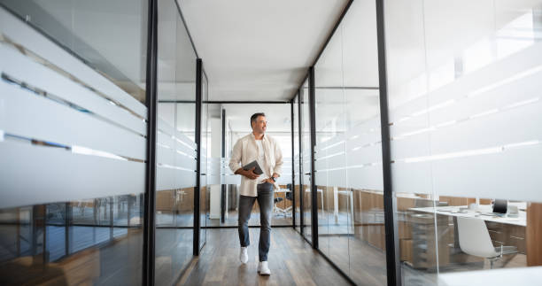 Mature professional executive business man walking, holding, using laptop pc or tablet at modern company office workplace space. Full body portrait of confident smiling senior businessman, copy space