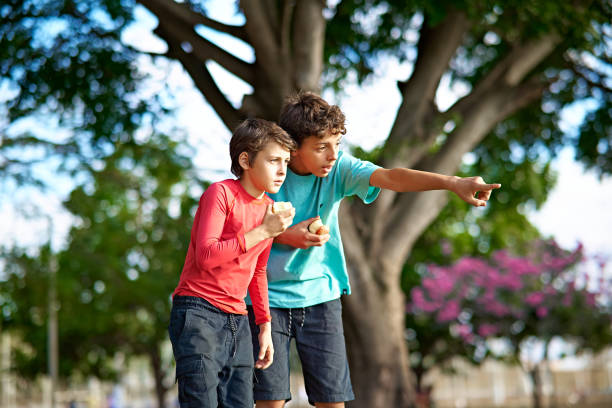 Portrait of two young boys, brothers, eating fruits in a public park.