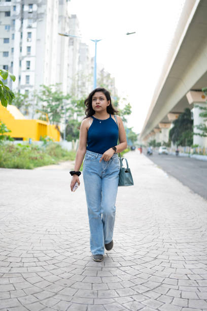 istock Woman in Blue Top and Jeans on a Tree-Lined Sidewalk 2158987379