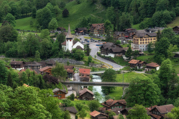 Quaint chapel atop a lush hill with majestic alpine mountains in the background. Peaceful rural landscape scene.K