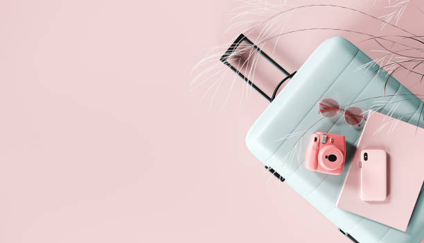 Blue luggage with travel accessories on pink background with copy space.