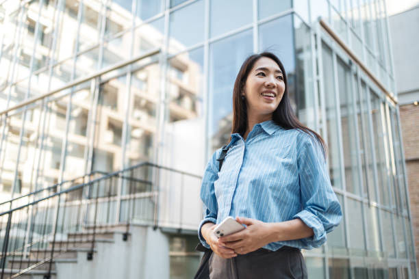 Asian woman smiling with smartphone while commuting in city.