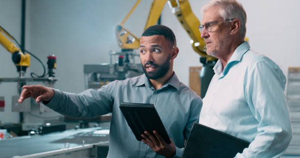 istock Talking, tablet or business people in robotics plant for production check or teamwork. Supervisor, manufacturing or process automation consultant with technology, machine or engineering inspection 2158997911