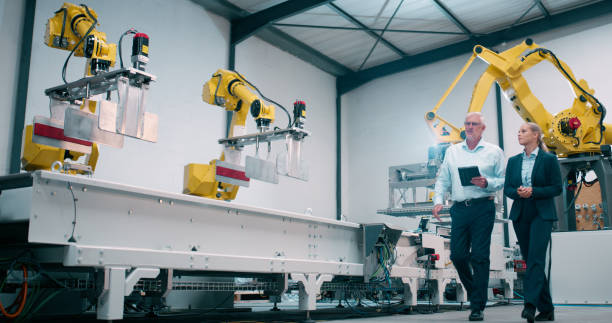 istock Robotics, teamwork and automation technician in factory for industry 4.0 and manufacturing inspection. Engineering woman or senior manager walking with digital tablet for technology at assembly line 2158997945