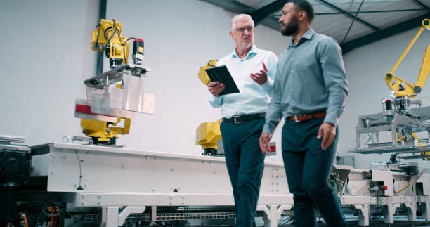 istock Robotics, machine and engineering team in factory for industry 4.0 and manufacturing inspection. Technician and senior manager walking with digital tablet for technology automation at assembly line 2158997948