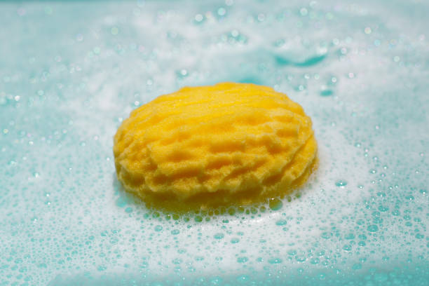 istock Yellow bath sponge floating on blue water with soap foam 2158999229