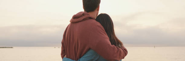 istock Young couple standing embracing on seascape background. Back view 2159004174