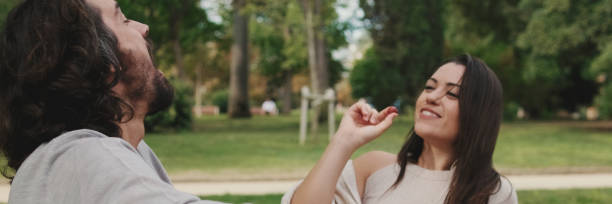 istock Happy smiling couple talking while sitting on blanket in park, panorama 2159004479