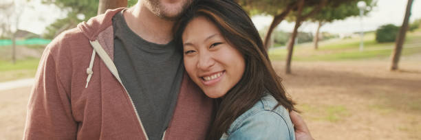 istock Close up, laughing couple hugging each other while standing in the park. looking at camera, panorama 2159004736