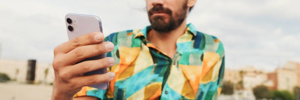 istock Young man sitting and using mobile phone on the beach, panorama 2159004900