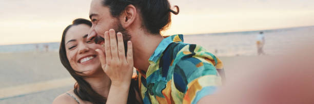 istock Laughing couple making video call while standing on the beach, panorama 2159005294