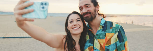istock Laughing couple taking selfie on mobile phone while standing on the beach, panorama 2159005342