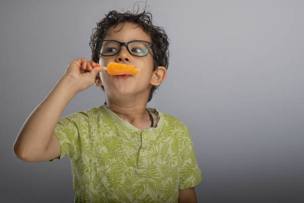 Cute boy eating flavored ice cream on gray background
