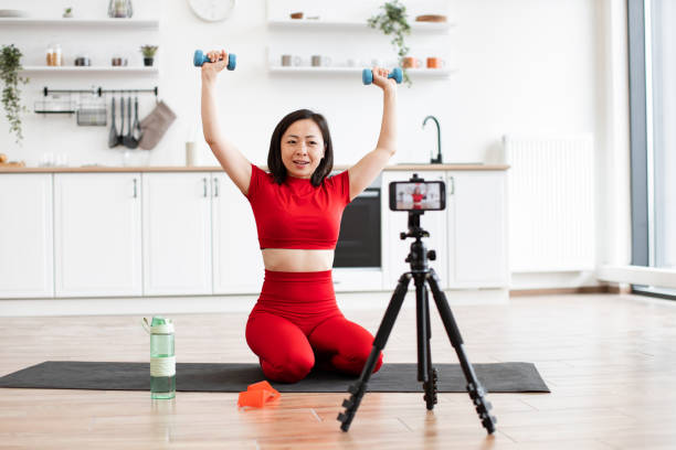 istock Woman recording workout session at home with dumbbells and tripod 2159010218