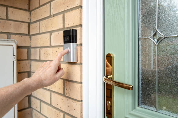 Visitor seen pressing the door bell button of a wireless smart home door bell which has an integrated camera and two-way audio. stock photo