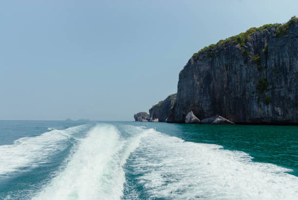 istock A boats wake cuts through turquoise waters toward a large island with steep cliffs and lush green foliage. The sky is clear, the sun shines bright 2159017049