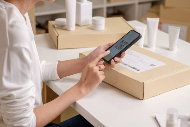 istock Asian e-commerce seller scan the QR code on package with smartphone, in a warehouse setting for an online beauty shop. 2159021960