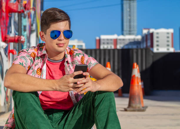 closeup shot of latin smiling young genz student, skater, art director, graphic designer, designer portrait enjoying his time in the united states while analysing finance data on digital devices with stock exchange market and his bank finance. - art basel miami beach immagine foto e immagini stock