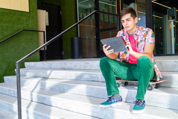 ritratto di giovane felice studente maschio dell'università del college latino che interagisce con la lettura della tecnologia e cerca alcune informazioni nella sua tavoletta digitale utilizzando la tecnologia 5g sul distretto di wynwood e sul distretto d - art basel miami beach immagine foto e immagini stock