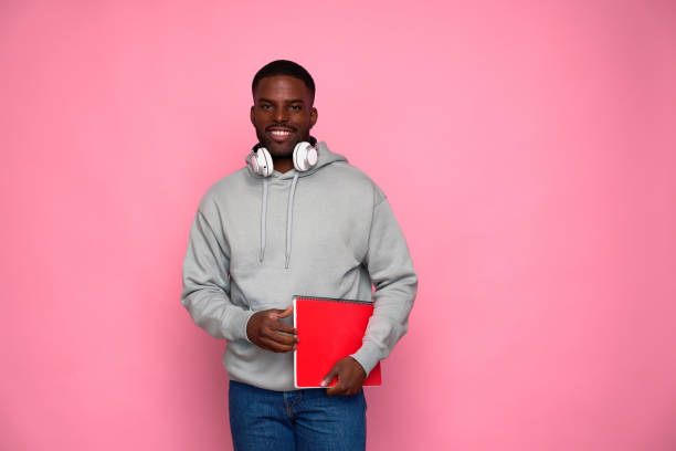 istock Young student smiling holding textbook wearing headphones on pink background 2159029877