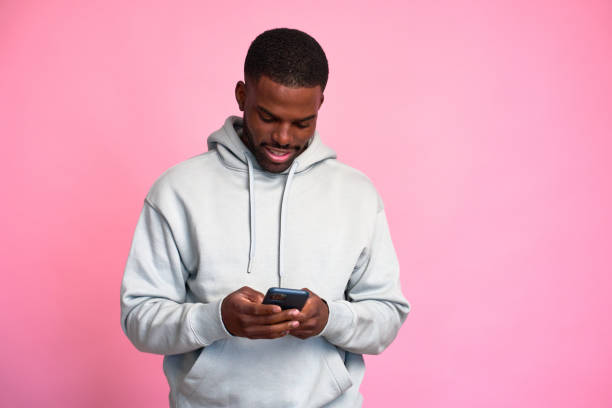 istock Young man smiling while texting on phone with pink background 2159029932