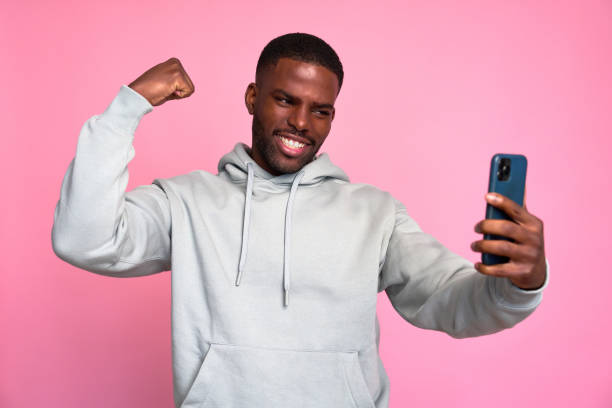 istock Young man celebrating success while taking selfie with smartphone 2159030121