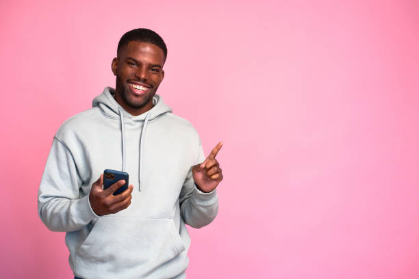 istock Young black man using smartphone and pointing aside on pink background 2159030309