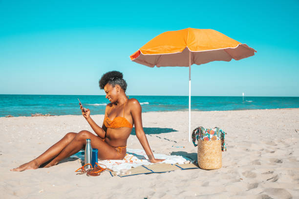 istock Woman sunbathing and texting on mobile on a sand beach 2159032833