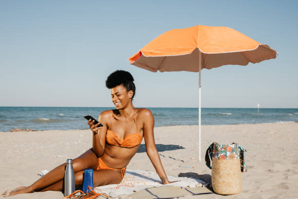 istock Woman sunbathing and texting on mobile on a sand beach 2159032850