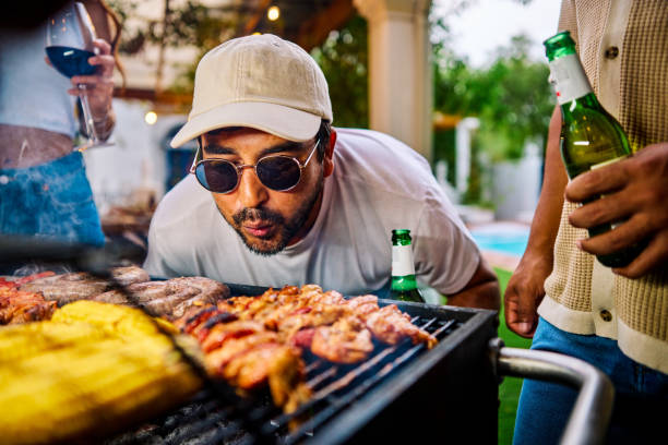 der mann, der den grill oder grill bekommt, wird durch das anblasen der kohlen angeheizt. geselliges beisammensein im freien. sommerküche und food-konzept. - grill zubereitung stock-fotos und bilder