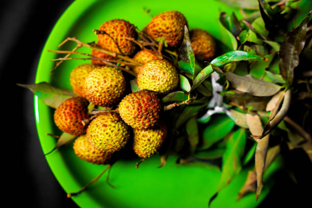Small ripe tropical lychee berries on a black plate on on the edge of the table, on a black background