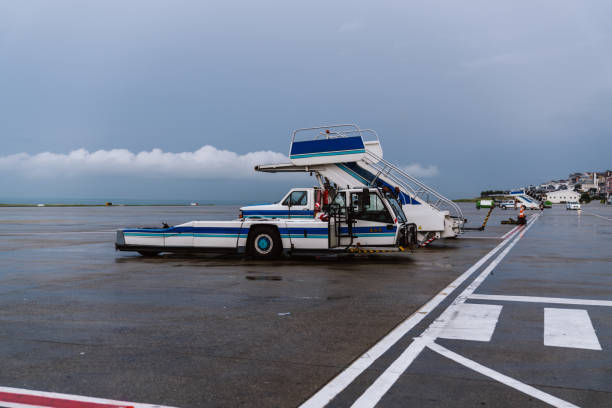 This photo captures the pre-flight preparation process of an airplane at the airport. The activities include refueling the aircraft, loading luggage, and positioning passenger stairs for boarding. The weather is cloudy and rainy, giving the runway a wet appearance. Ground service vehicles and personnel are actively involved in these operations.