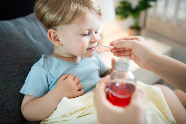 Mother giving medicine cough syrup to her little son at home. Young mother giving medicine cough syrup to her little son at home. child liquid medicine stock pictures, royalty-free photos & images