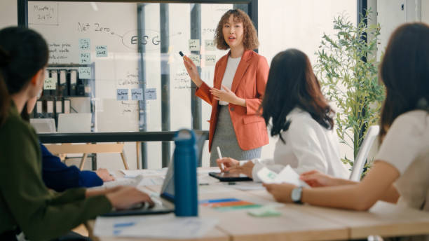 Team Discussing ESG Strategies in a Modern Office A diverse team of professionals in a modern office, engaged in a discussion about ESG (Environmental, Social, and Governance) strategies, with a presenter pointing at a whiteboard. sustainable business stock pictures, royalty-free photos & images