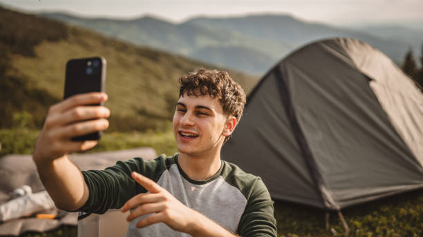 istock Young boy sit in front tent and video call or selfie on the mountain 2159051470